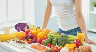 IStock / Imagem de mulher parada em frente a mesa repleta de alimentos saudáveis